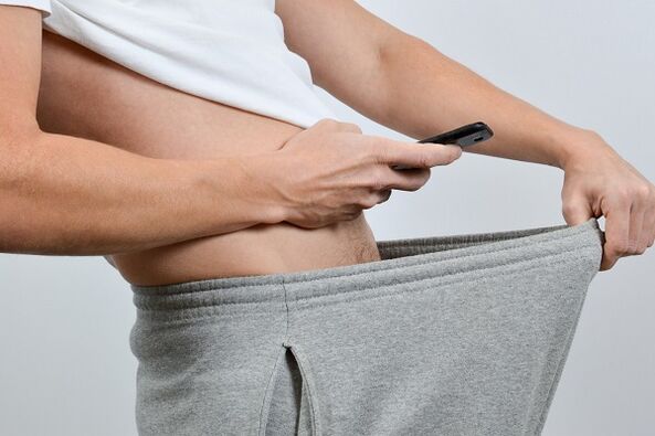 Bir kishi kattalashgan jinsiy olatni uning shimlarini pastga qaradi